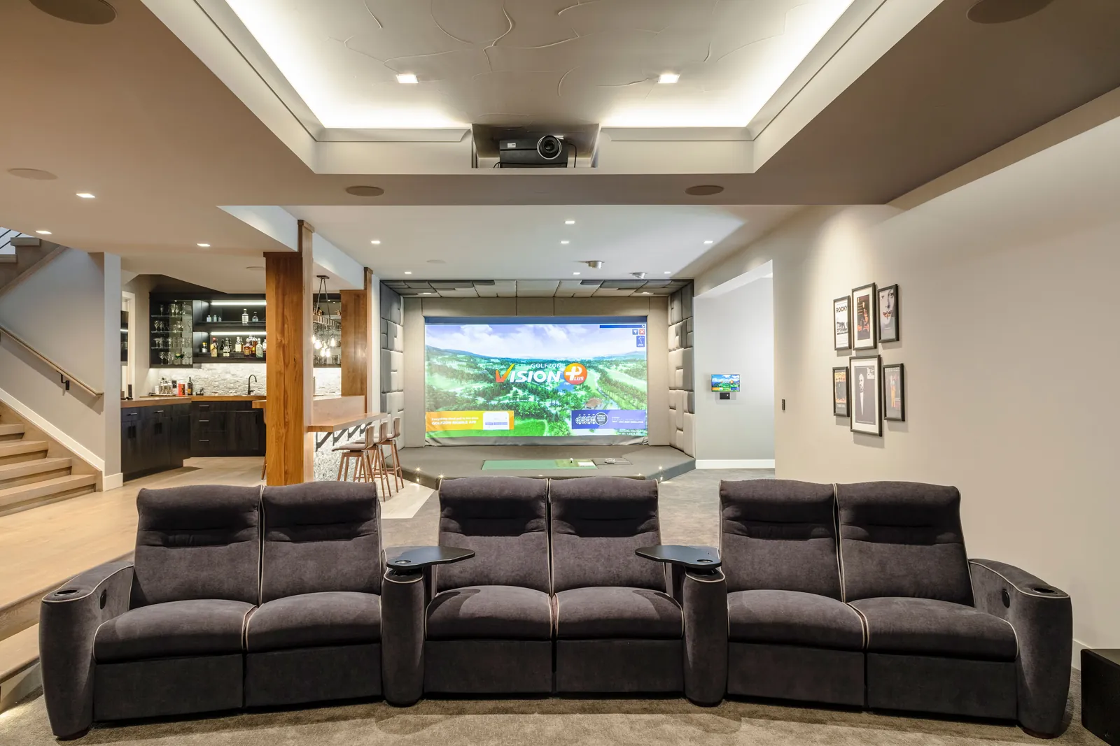 A finished basement with theater recliners facing a golf simulator bay, timber columns, and a bar