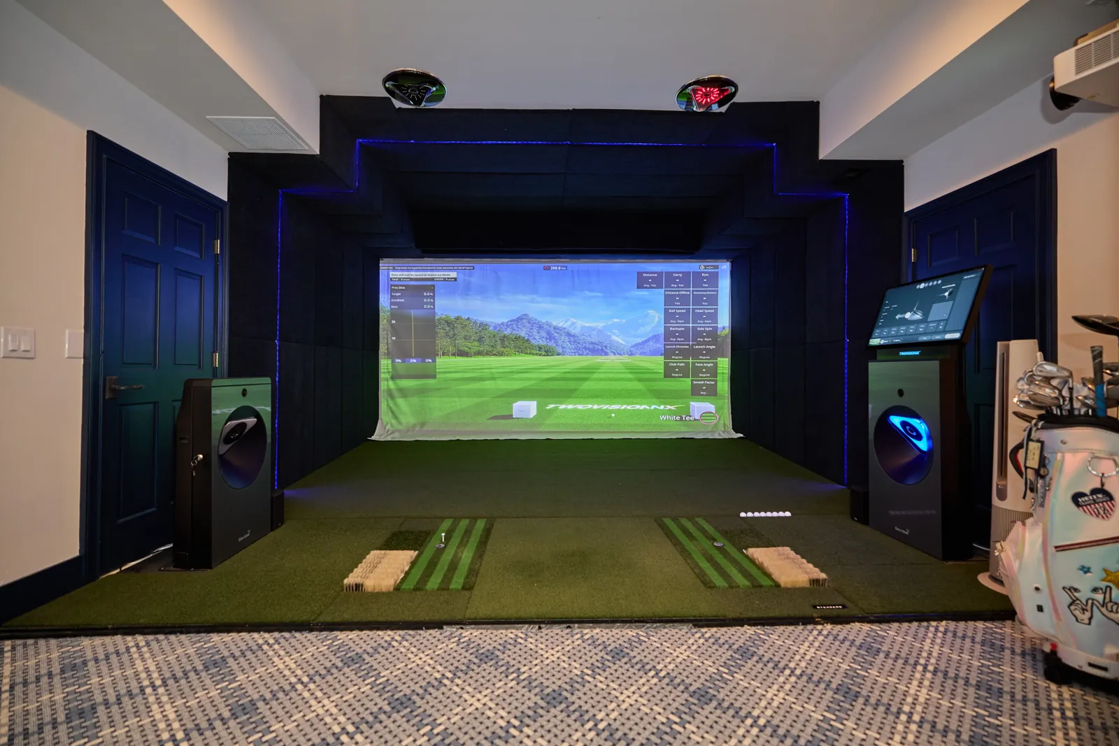 A golf simulator bay with a mountain course on the screen and hitting mats on the floor