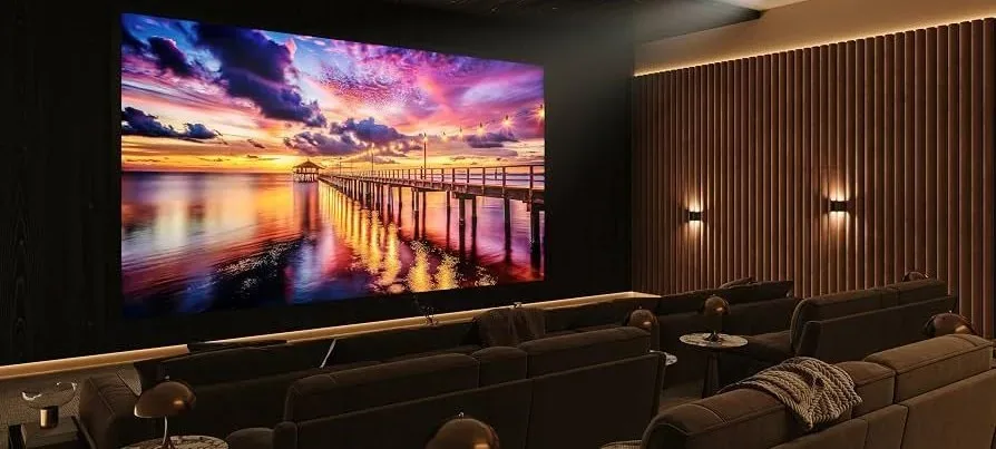 A large screen showing a sunset in a dark theater with wood slat walls and sconces