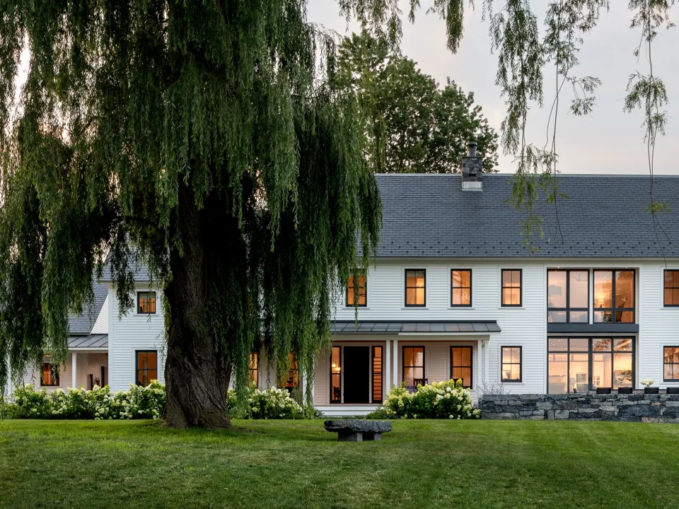 The Cornwall farmhouse at dusk behind a willow, lights on inside