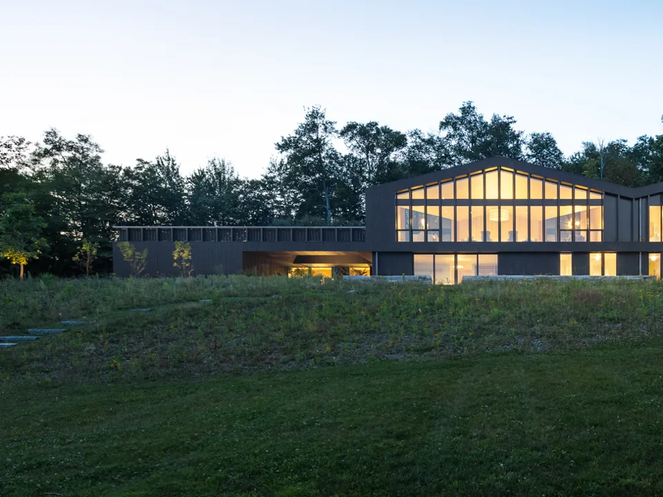 Ridgeline at dusk, its upper floor glowing above a meadow in Stowe